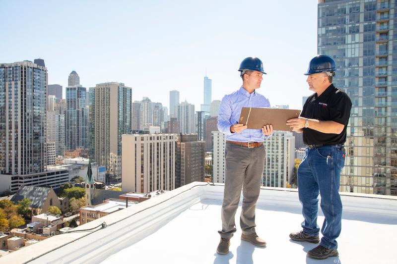 Two men in hard hats inspecting a commercial roof