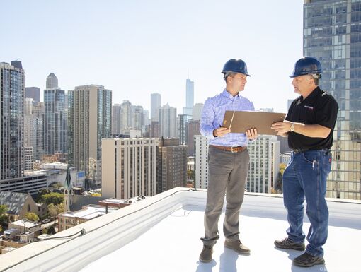 Two men in hard hats inspecting a commercial roof