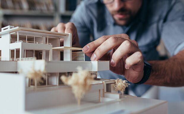 Close up of male architect hands making model house. Man architect working in the office.