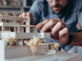 Close up of male architect hands making model house. Man architect working in the office.