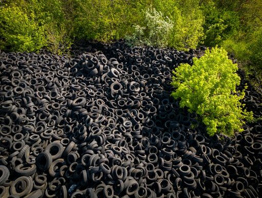 Aerial view of the stark contrast between a massive landfill of used car tires and the surrounding green trees. Tire dump showcases human waste impact on environment.